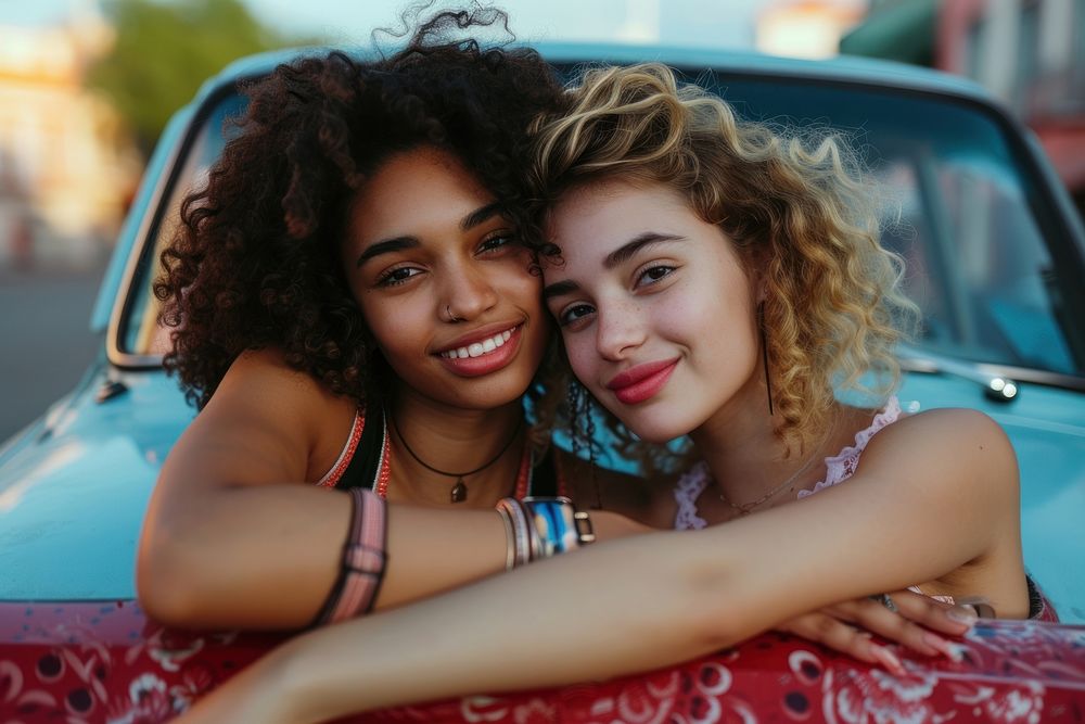 Woman with arm around female friend leaning on car smile togetherness affectionate.