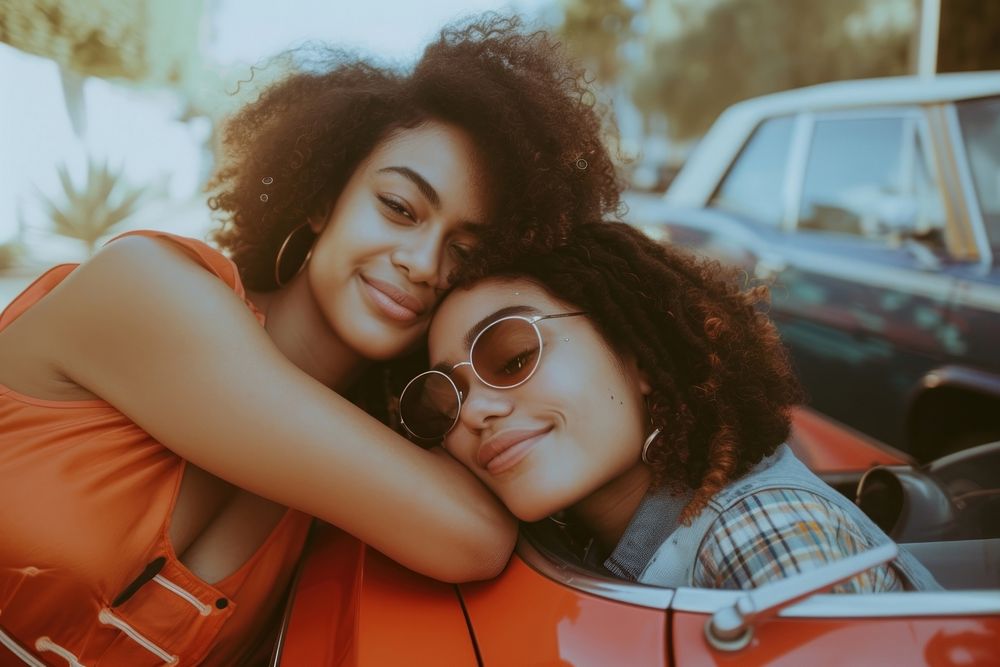 Woman with arm around female friend leaning on car vehicle glasses hugging.