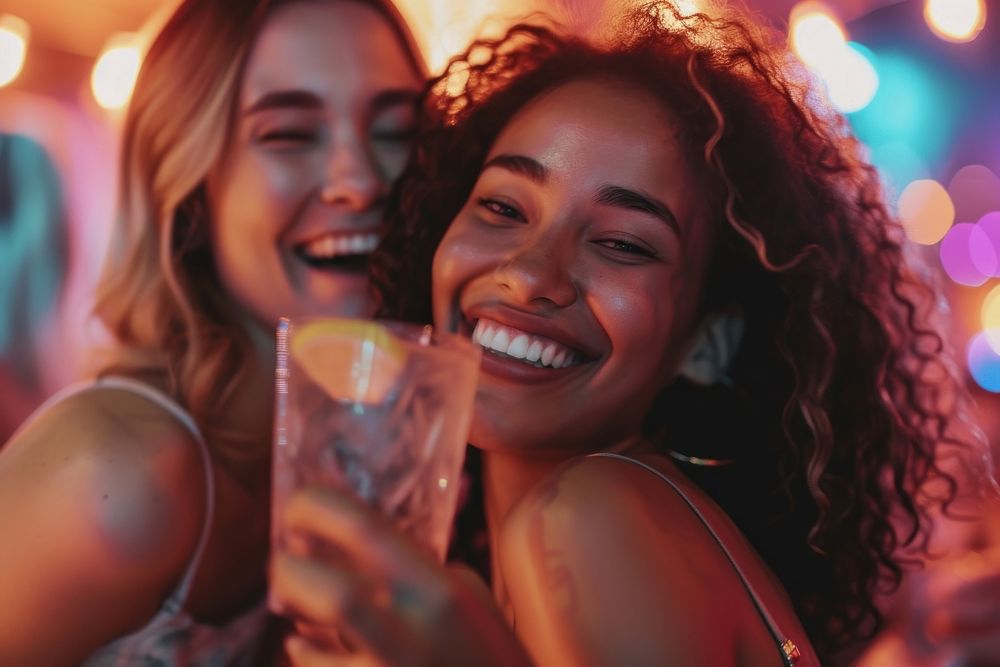 Carefree young woman with drink dancing by female friend enjoying at nightclub carefree laughing smile.
