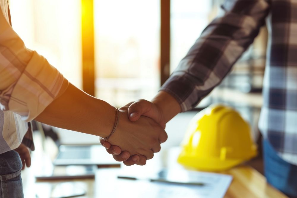Two architects people shaking hands in front of yellow hard hats on desk hardhat adult construction.