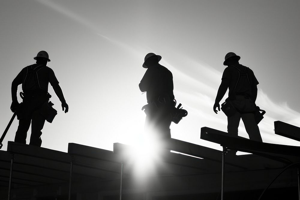 Four construction workers inspecting an under construction home silhouette outdoors hardhat.