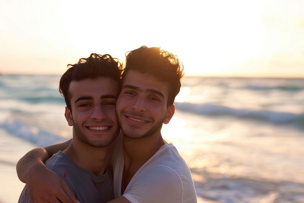 Middle eastern gay couple hugging on the beach portrait outdoors smiling.