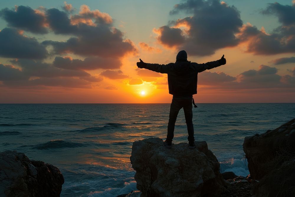 Young Palestinian man arms outstretched sea outdoors horizon.