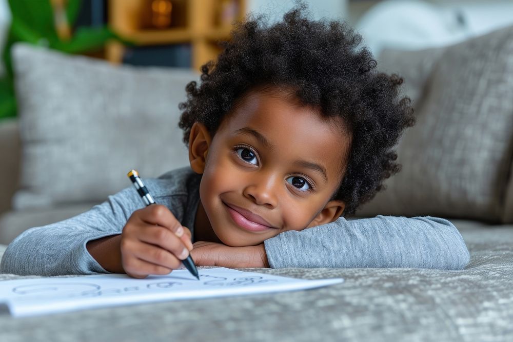 African american kid boy laying at the sofa writing child pen.
