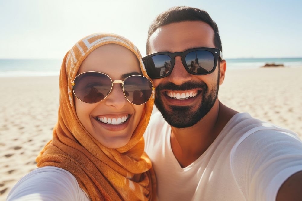 Middle eastern man and woman taking a selfie at the beach sunglasses portrait outdoors.