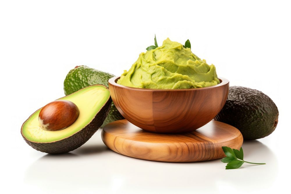 Guacamole in a wooden bowl and avocado fruits on the side plant food white background.