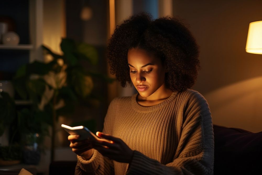 Young Black woman managing online banking with smartphone sitting on the sofa at home light adult head.