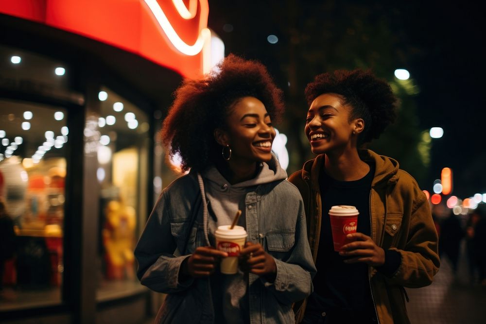 Two young black women laughing drinking street.
