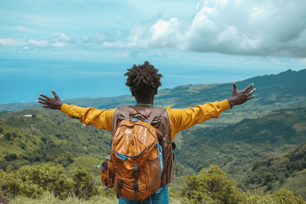 Young Ethiopian man with backpack open arms in the mountains with view of ocean adventure outdoors nature.