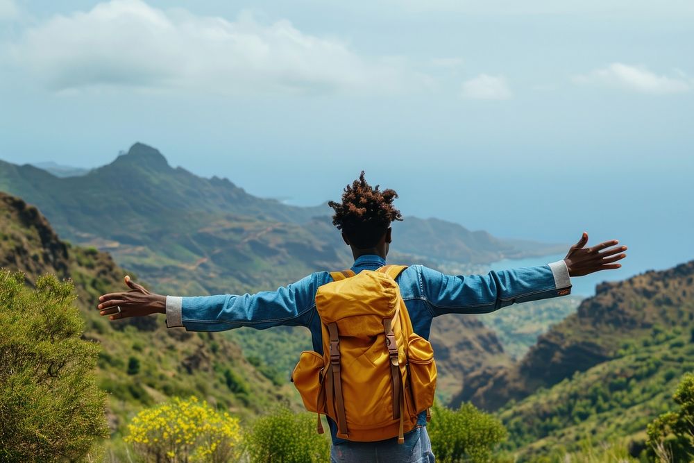 Young Ethiopian man with backpack open arms in the mountains with view of ocean backpacking tranquility wilderness.