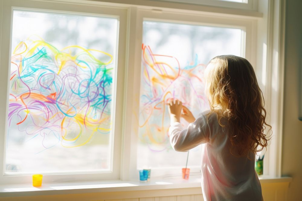 Girl using marker to paper rainbow on the window child transparent paintbrush.