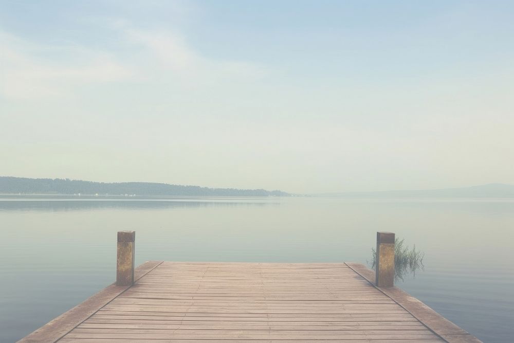 Long wooden pier on a smooth lake landscape outdoors horizon.