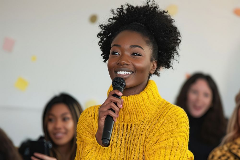 An african american woman wearing yellow sweater holding up microphone speaking in a conference smile adult women.