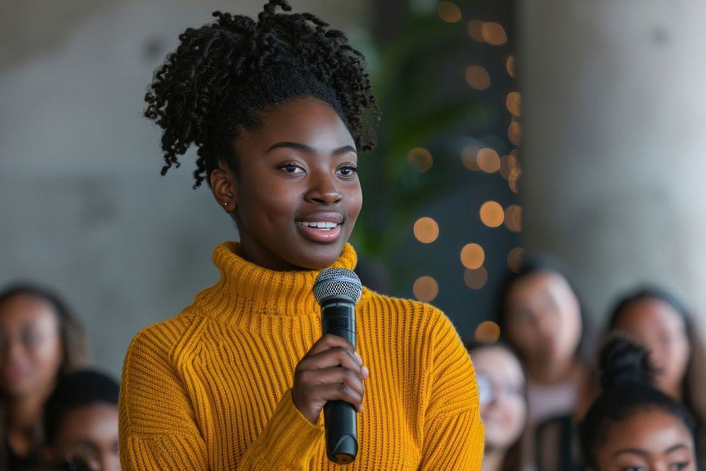 An african american woman wearing yellow sweater holding up microphone speaking in a conference adult women togetherness.