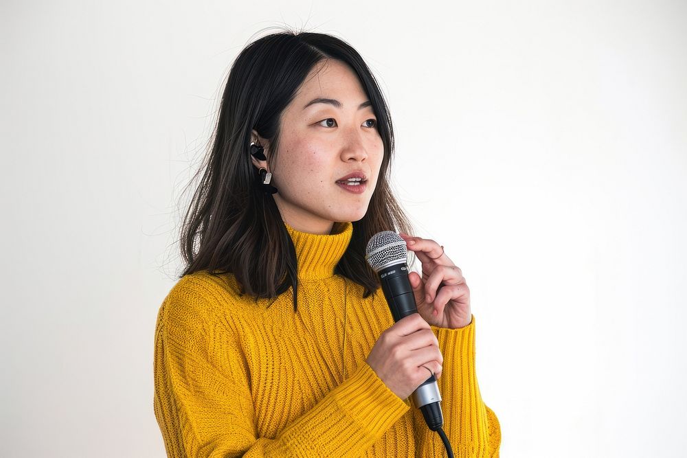 An asian woman wearing yellow sweater holding up microphone speaking in a conference adult women white background.