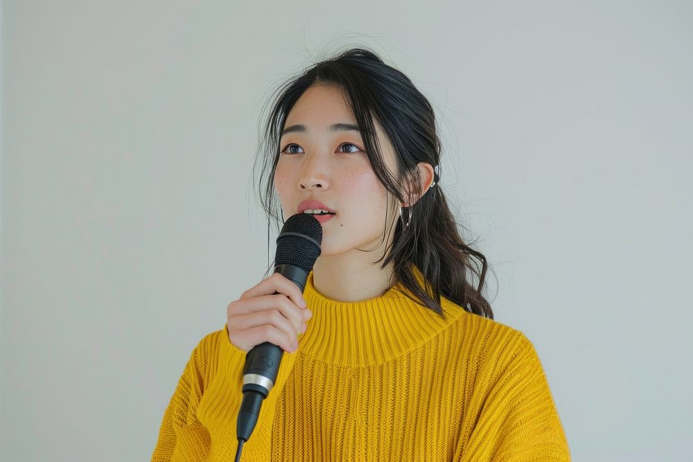 An asian woman wearing yellow sweater holding up microphone speaking in a conference adult women performance.