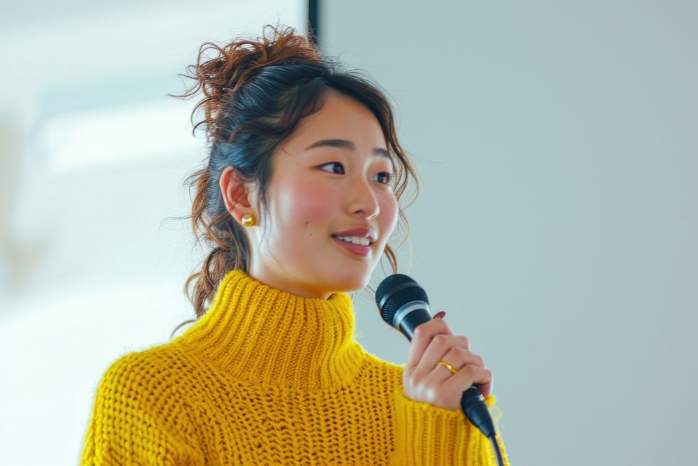 An asian woman wearing yellow sweater holding up microphone speaking in a conference adult women hairstyle.