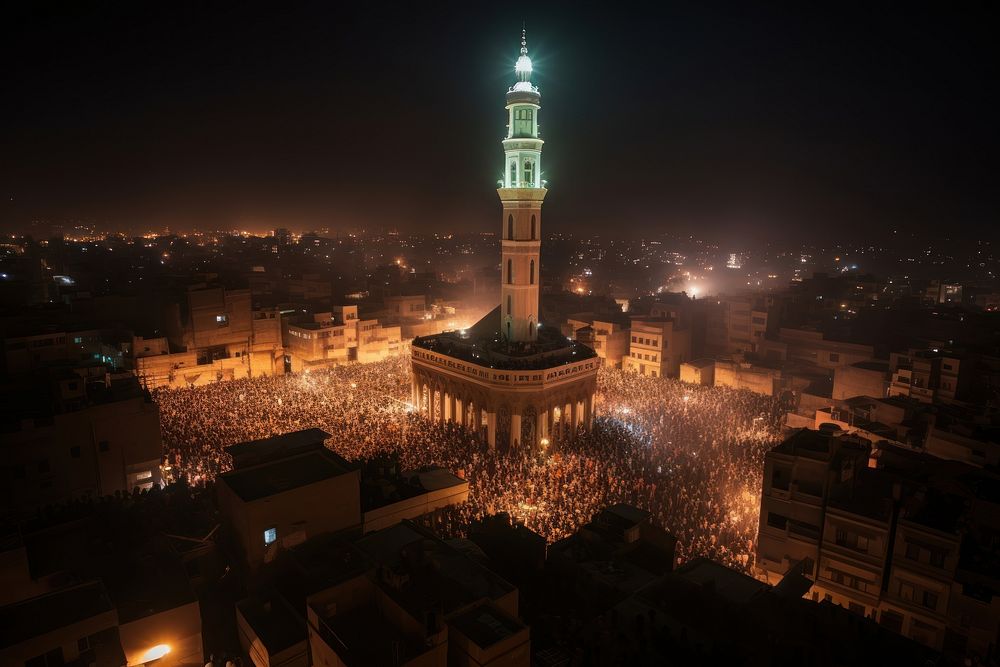 Huge crowd gathered around minaret architecture illuminated cityscape.