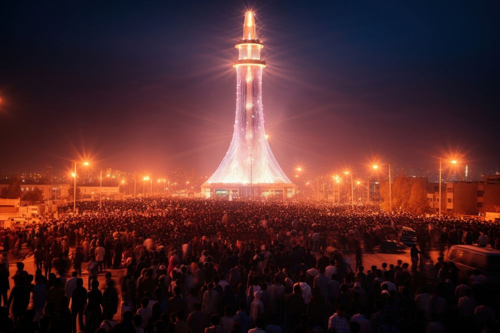 Huge crowd gathered around minaret architecture illuminated landmark.