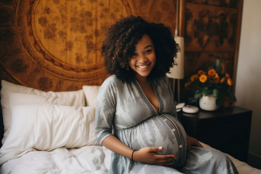 Young black woman sits on bed holding pregnant belly adult happy anticipation.