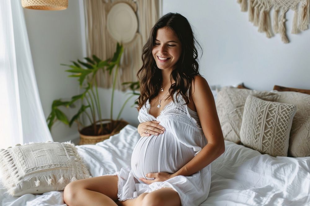 Young woman sits on bed holding pregnant belly furniture sitting adult.