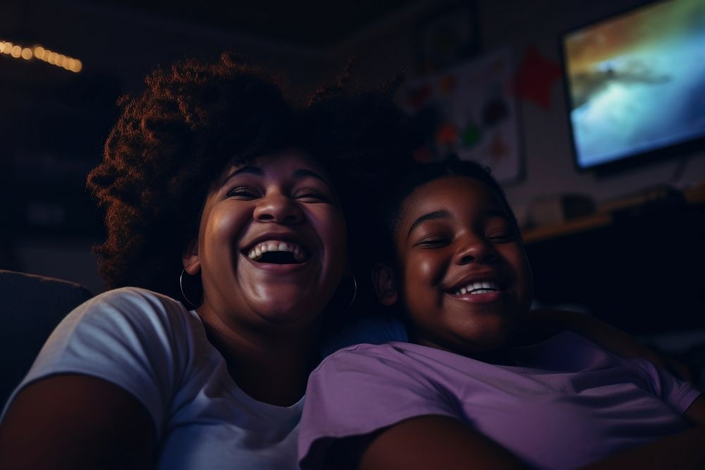 Daily life of black mom and daughter wacthing TV in the room laughing family adult.