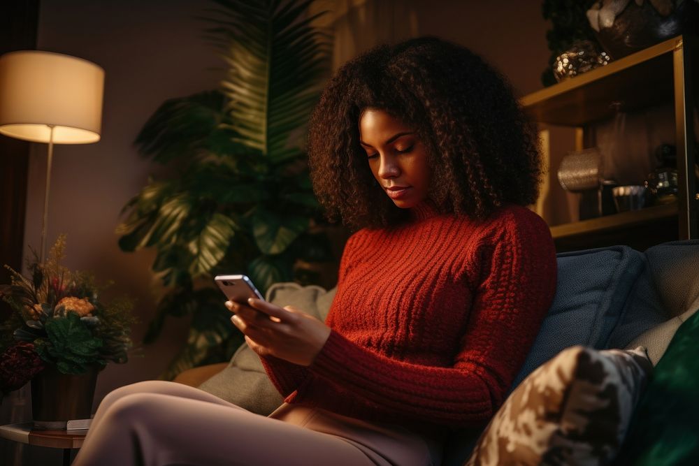 Young Black woman managing online banking with smartphone sitting on the sofa at home adult head portability.