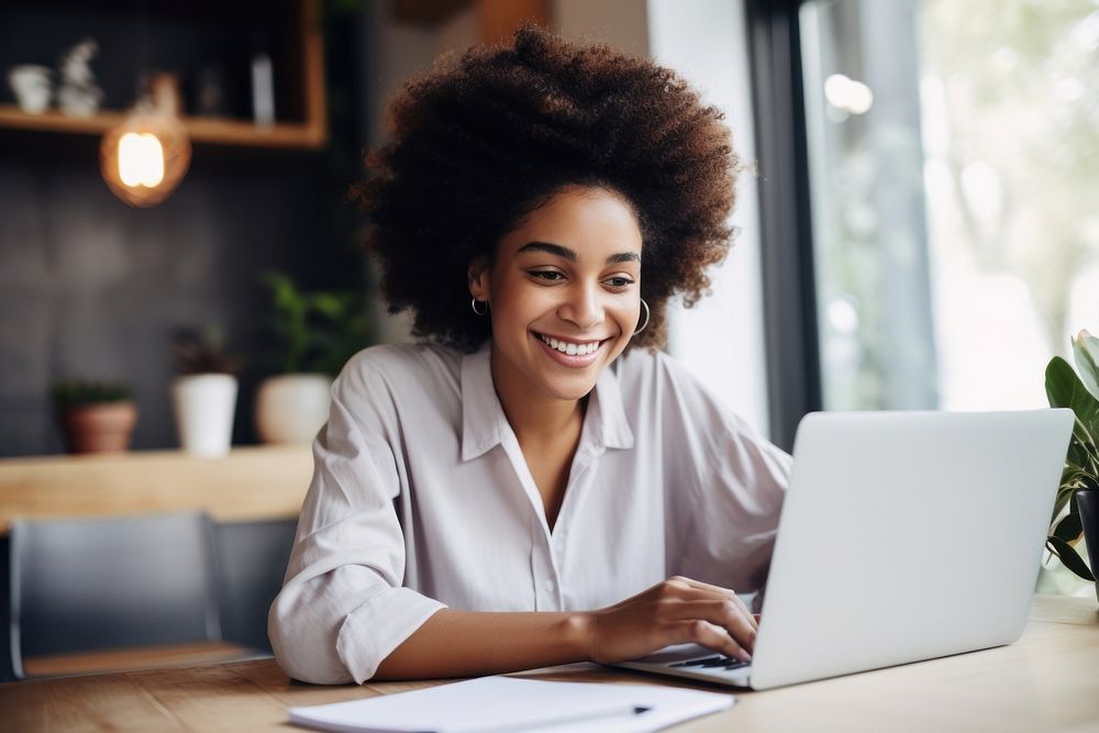 Black woman sitting at desk working on laptop computer smiling adult.