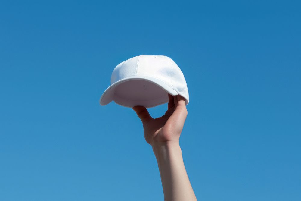 Hands holding a white baseball cap hand blue sky.