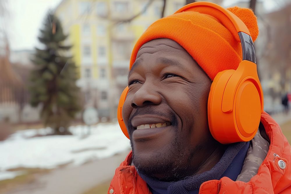 Happy young black man enjoying music listening through wireless headphones on footpath portrait adult smile.