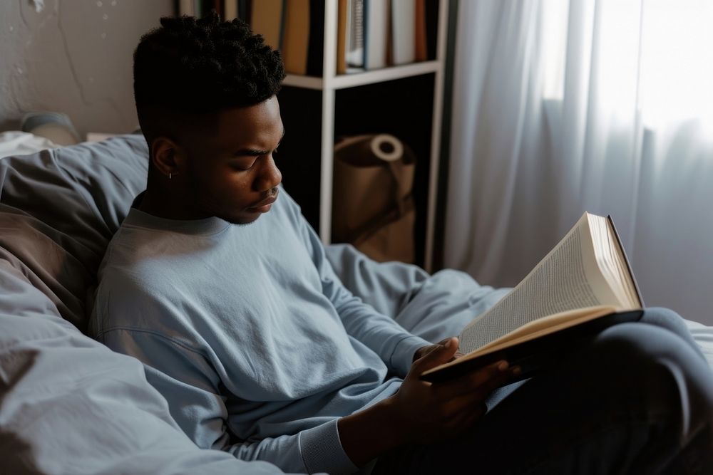 African American young man reading sitting bedroom.
