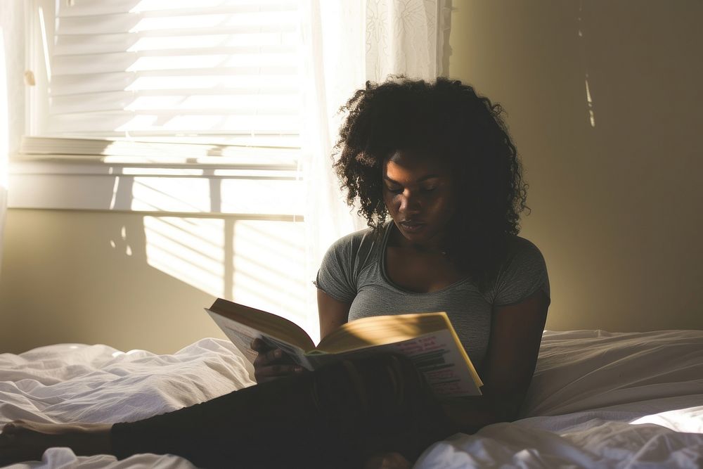 African American young woman reading book bed.