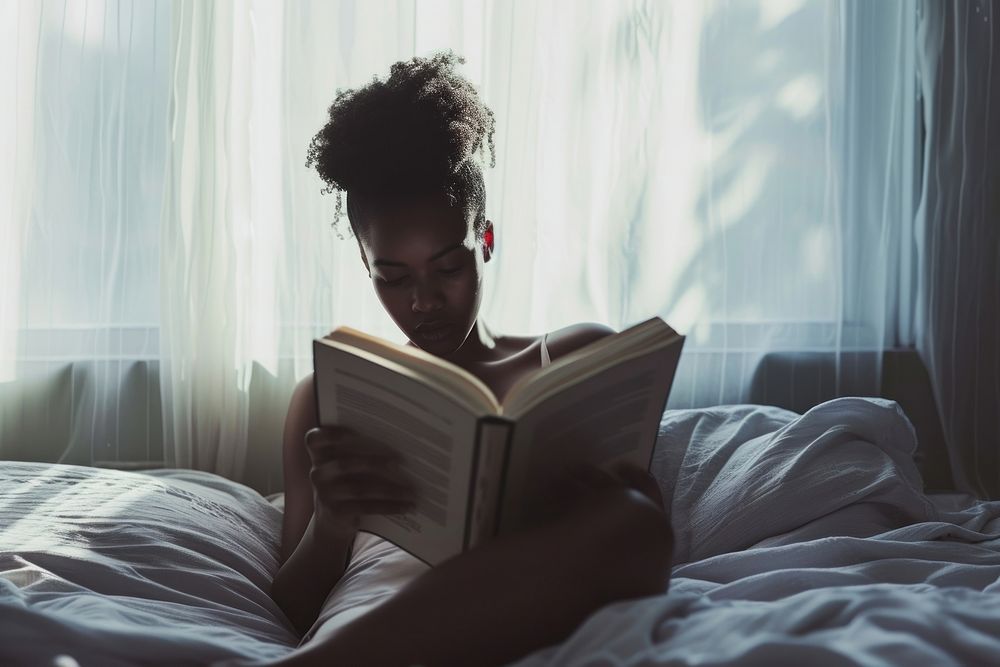 African American young woman reading book bed.