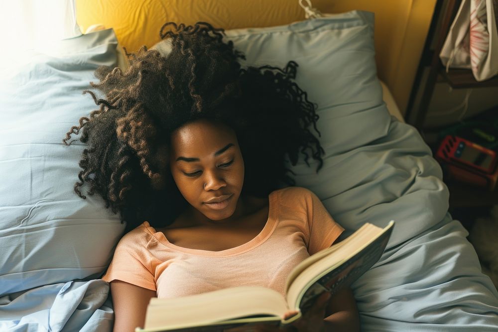 African American young woman reading bedroom book.