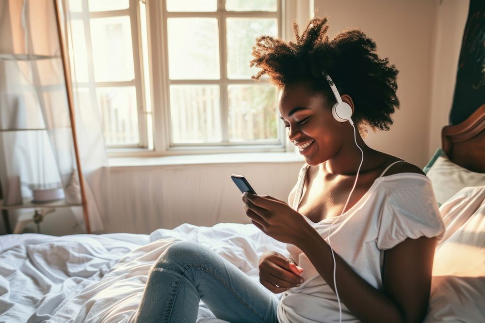 African American young woman headphones sitting bedroom.