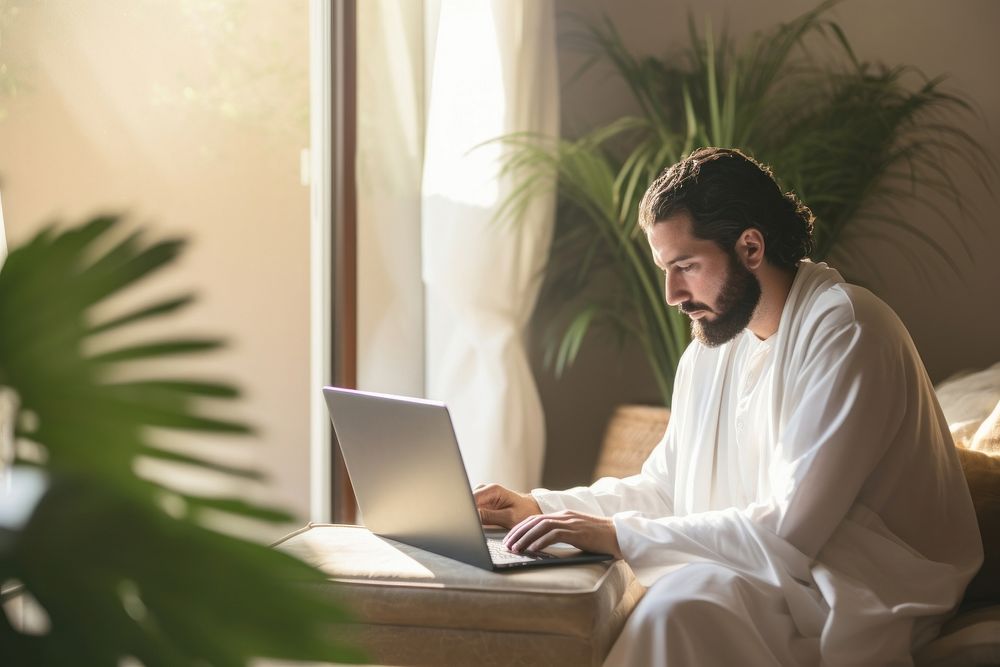 Middle eastern man in thawb typing on his laptop computer sitting adult.