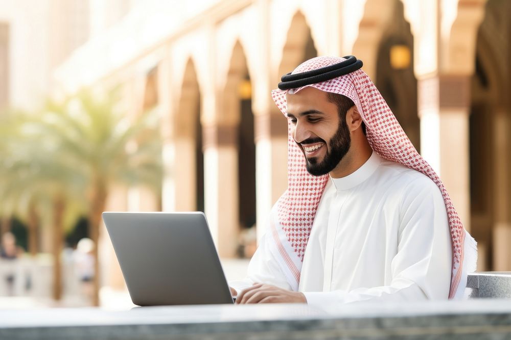 Middle eastern man in thawb typing on his laptop computer people architecture.