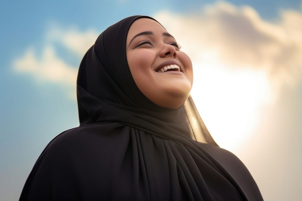 Plus size Middle eastern teen woman in abaya and hijab laughing outdoors looking.