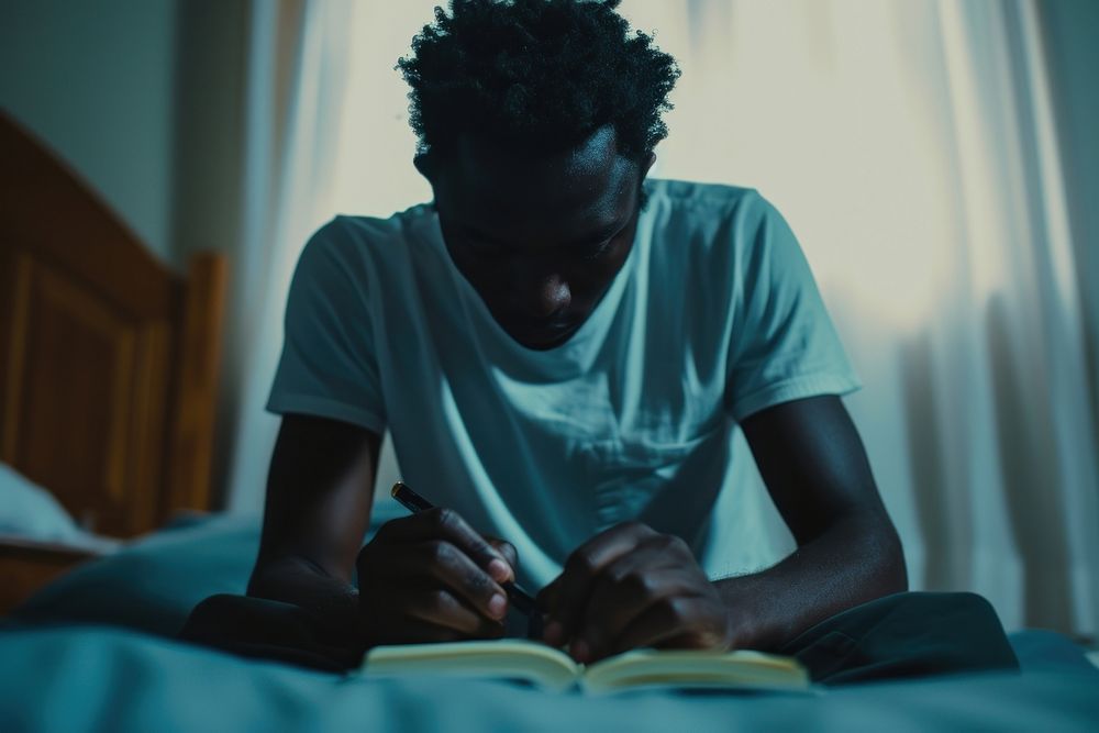 Black man writing reading bedroom.