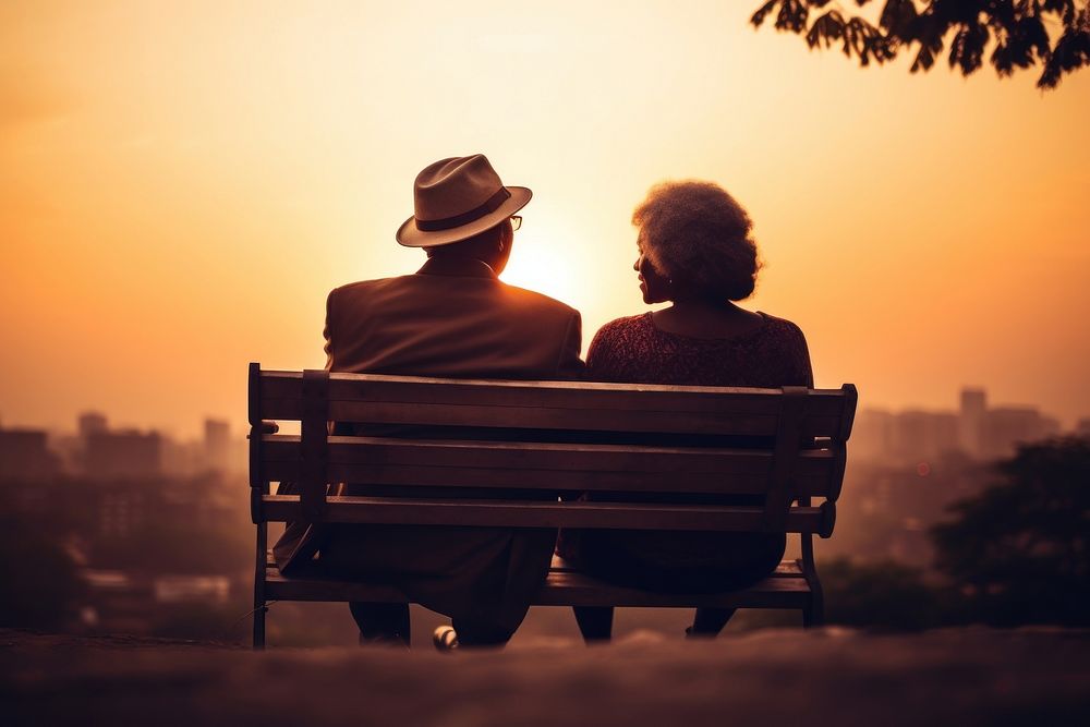 Senior black couple sitting sunset bench.