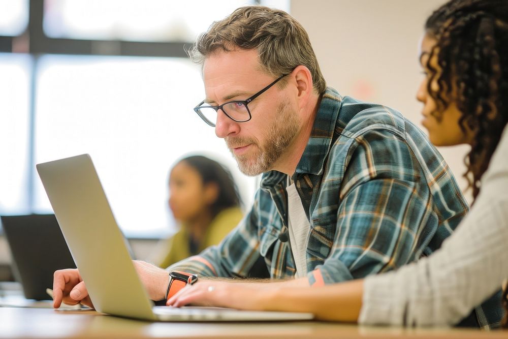 Professor assisting college student laptop classroom computer.