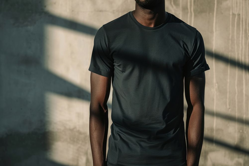 Black man wearing t-shirt standing with clean concrete background sleeve architecture midsection.