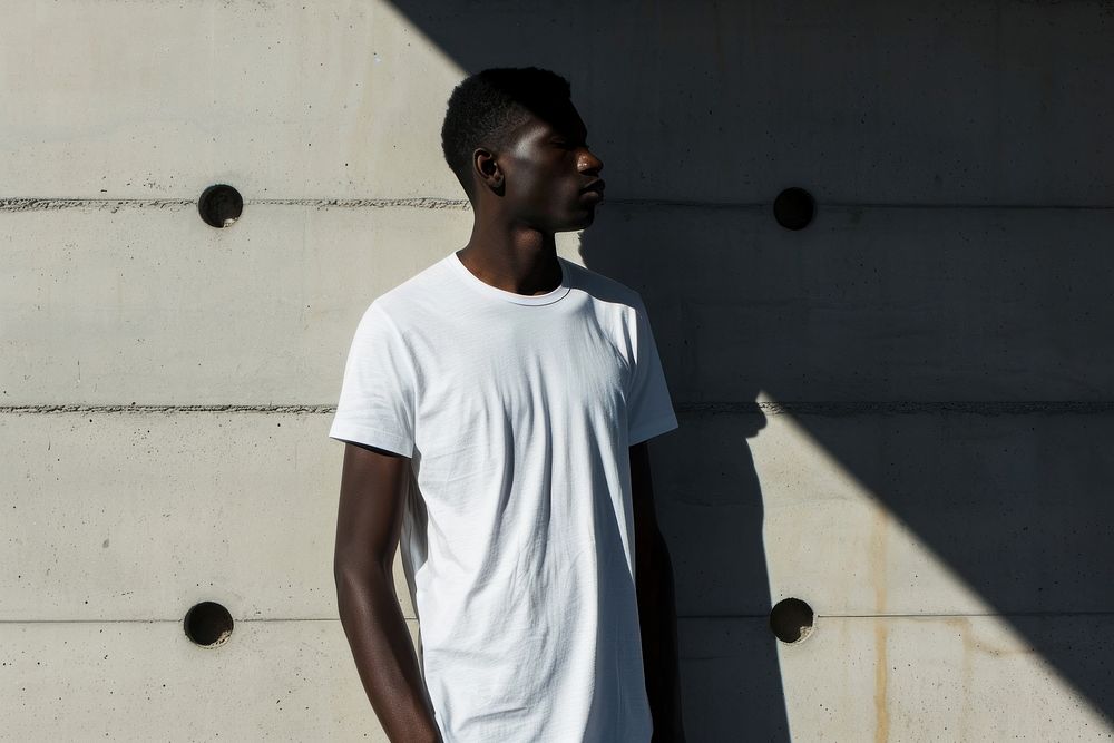 Black man wearing t-shirt standing with clean concrete background shadow contemplation architecture.
