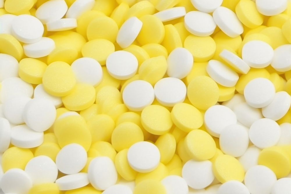 White pills or capsules lies in rows diagonal on yellow background backgrounds white confectionery. AI generated Image by…