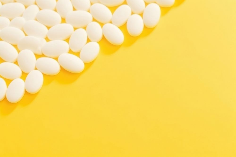 White pills or capsules lies in rows diagonal on yellow background backgrounds white medication. AI generated Image by…