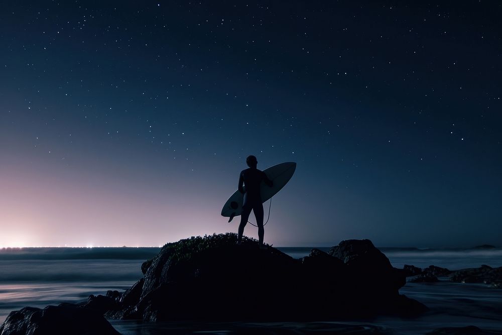 Surfer on rock looking at ocean night outdoors surfing.