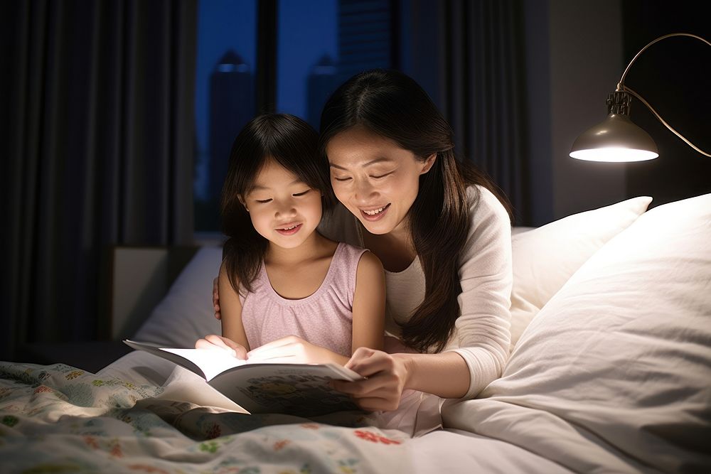 Mother and daughter reading book at night on a bed publication furniture light.