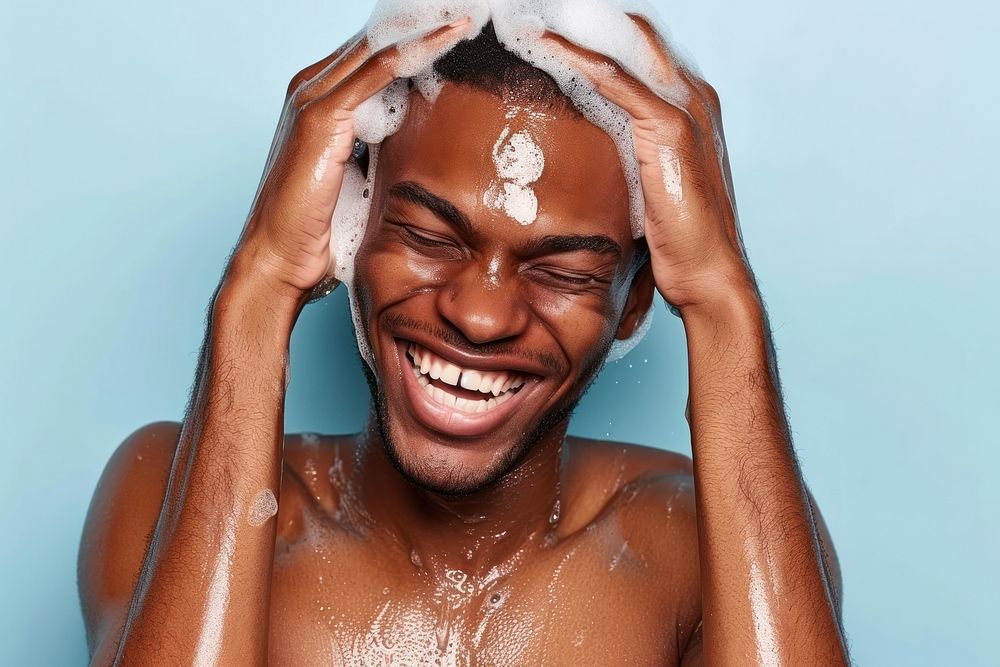 A happy black guy washing hair bathing barechested relaxation.