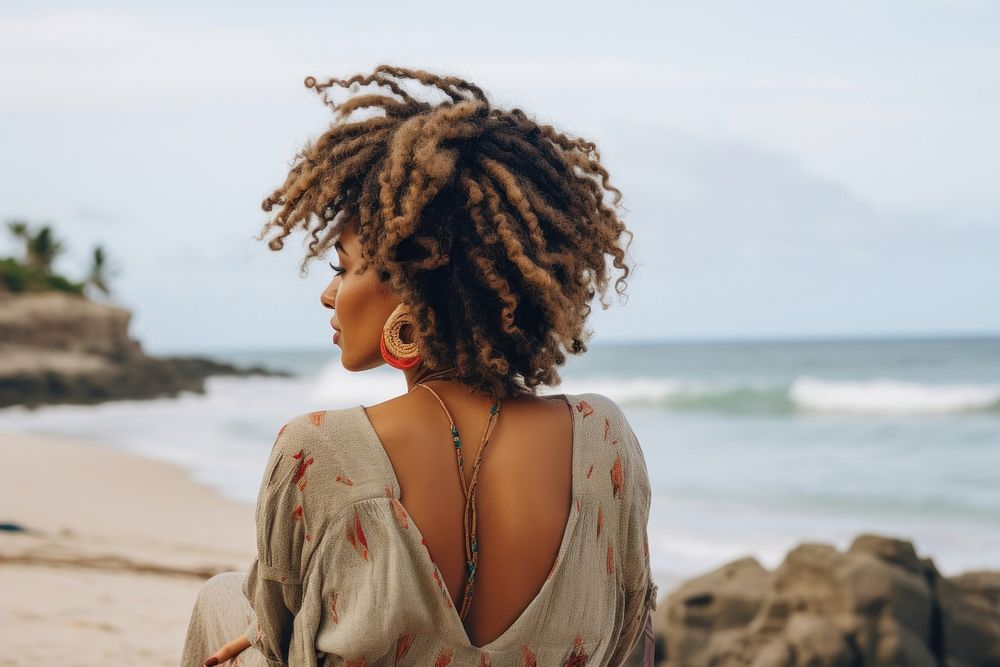 An African american woman with dreadlock hair sitting relaxed on a beach looking at the sea dreadlocks summer adult.