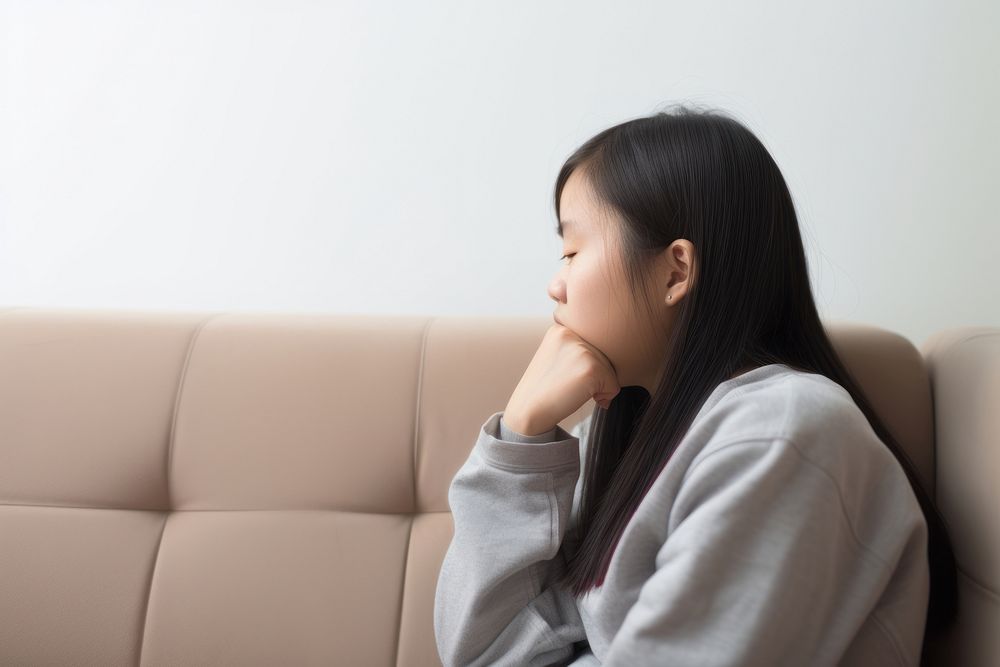An east asian teenager suffering from sickness worried sitting sofa.